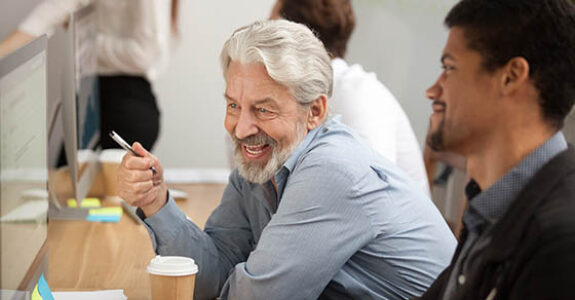 Smiling,Senior,Employee,Discussing,Email,With,African,Colleague,At,Workplace,